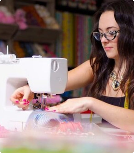 Woman using a sewing machine in a craft room with colorful materials in the background