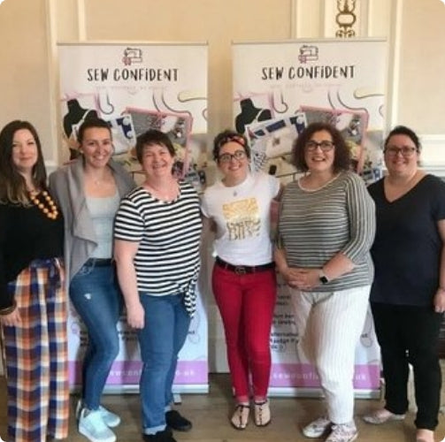 Group of women posing together with 'Sew Confident' banners in the background